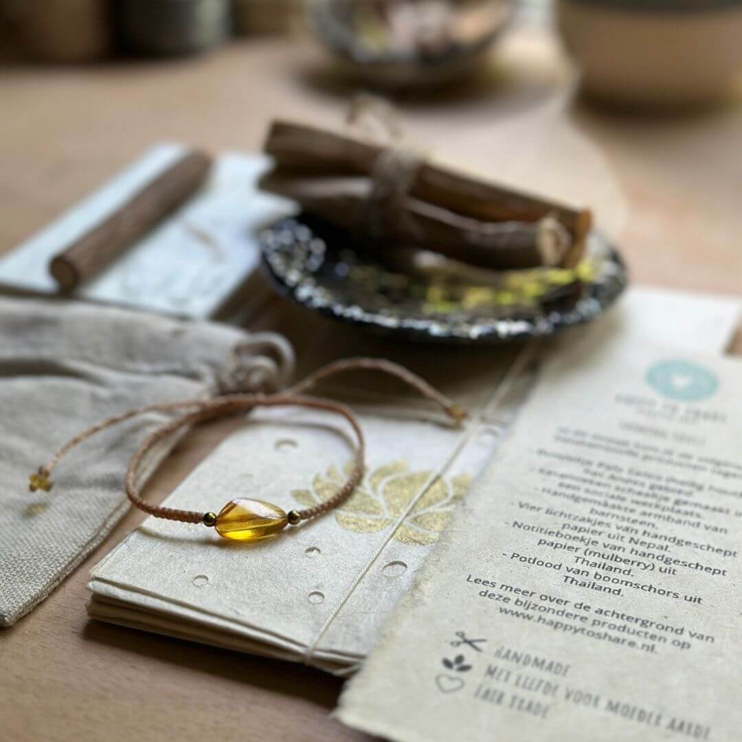 Geschenkbox van graskarton met kraft bruin vloeipapier, keramieken schoteltje met palo santo, barnsteen armband, lichtzakjes, notitieboekje, potlood en mandala kaart.