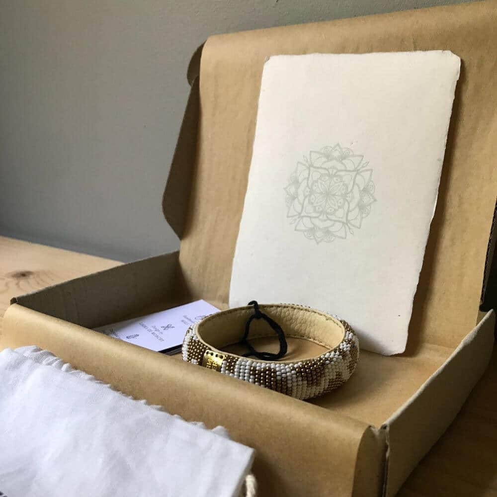 Een eerlijk cadeau met een goud en wit kleurige beaded bracelet armband van Return to Sender in een doosje van graskarton met een wit katoenen zakje en mandala kaart van handgeschept papier.