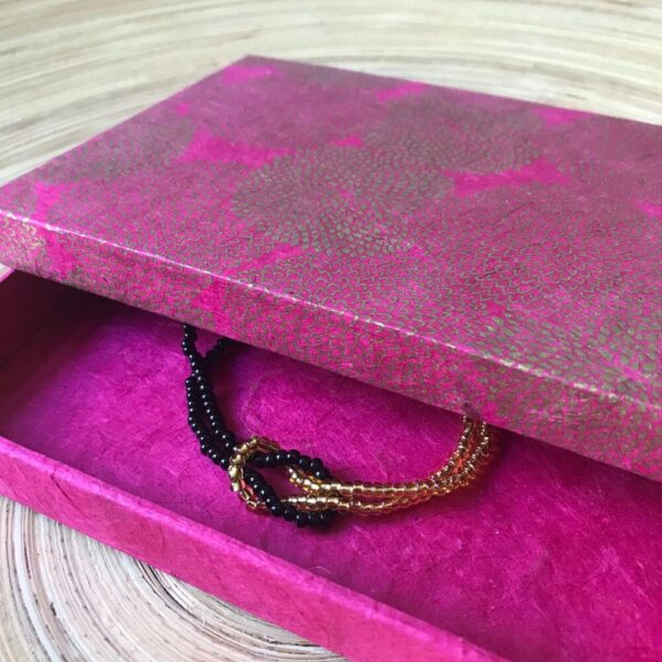 Zwart en goud kleurige infinity armband met een roze en goud kleurig sieradendoosje van handgeschept papier.
