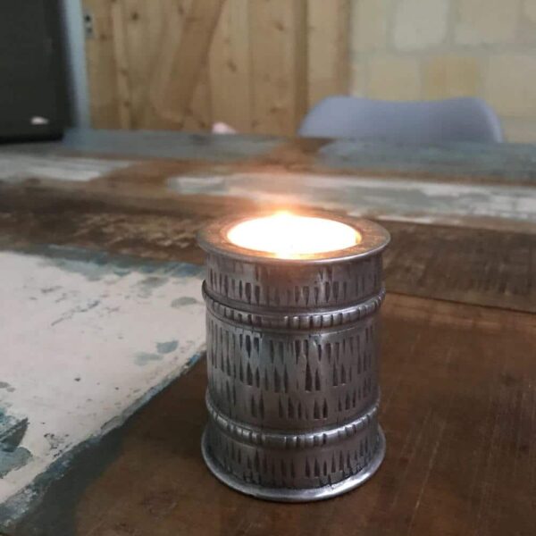 Aluminium kaarsenhouder met brandend theelichtje op scrap wood tafel.