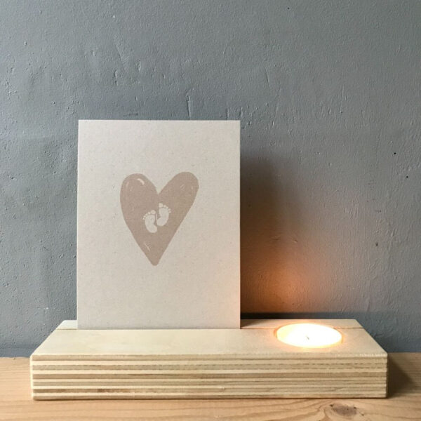 Blank houten kaartenhouder met brandend theelichtje en vezelrijke ecru kleurige kaart met lichtroze hart en ecru kleurige babyvoetjes.