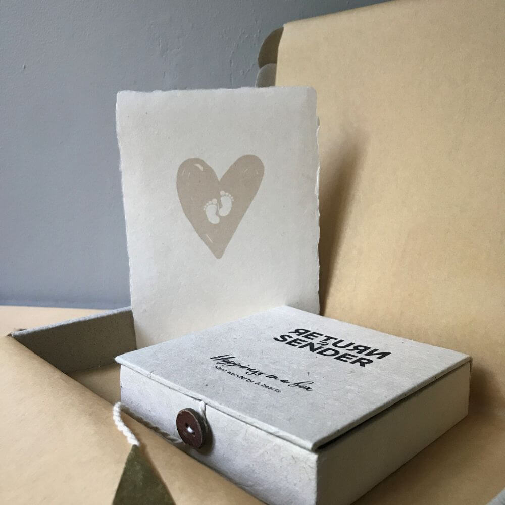 Ecru kleurig happiness in a box doosje van handgeschept papier in een cadeau doosje met kraft bruin zijdepapier.tter op blank houten tafel met brandend kaarsje en bloemenvaasje.