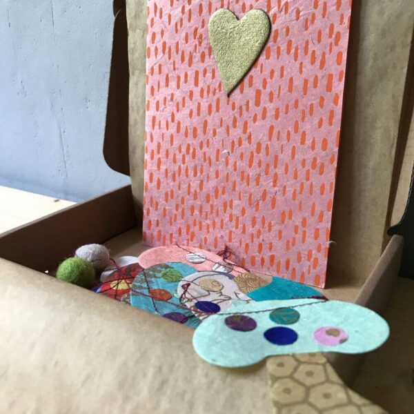 Paddestoelen slinger van handgeschept papier in cadeau doosje met kraft vloeipapier en roze kaart met gouden hartje.
